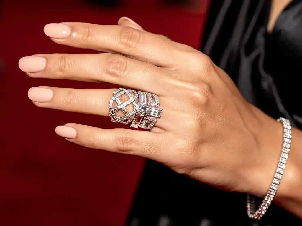 Celebrity hand showcasing intricate diamond ring and bracelet on red carpet.